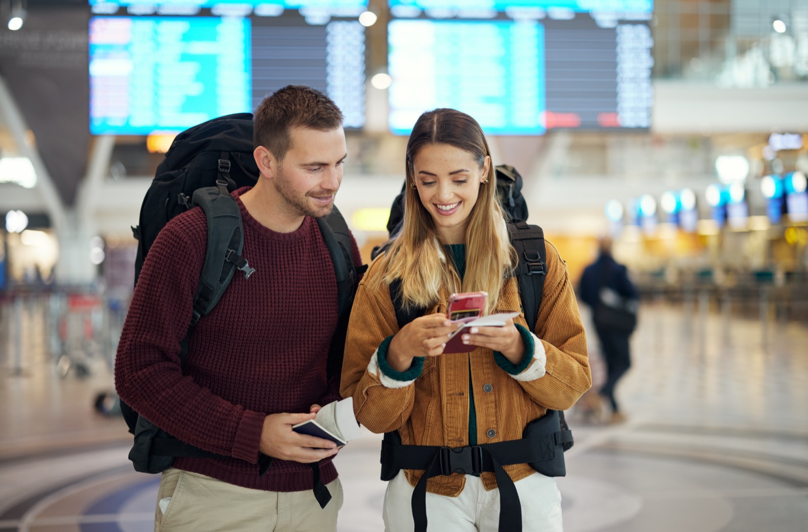 Reisepaar mit Rucksäcken checkt am Flughafen die Reiseunterlagen